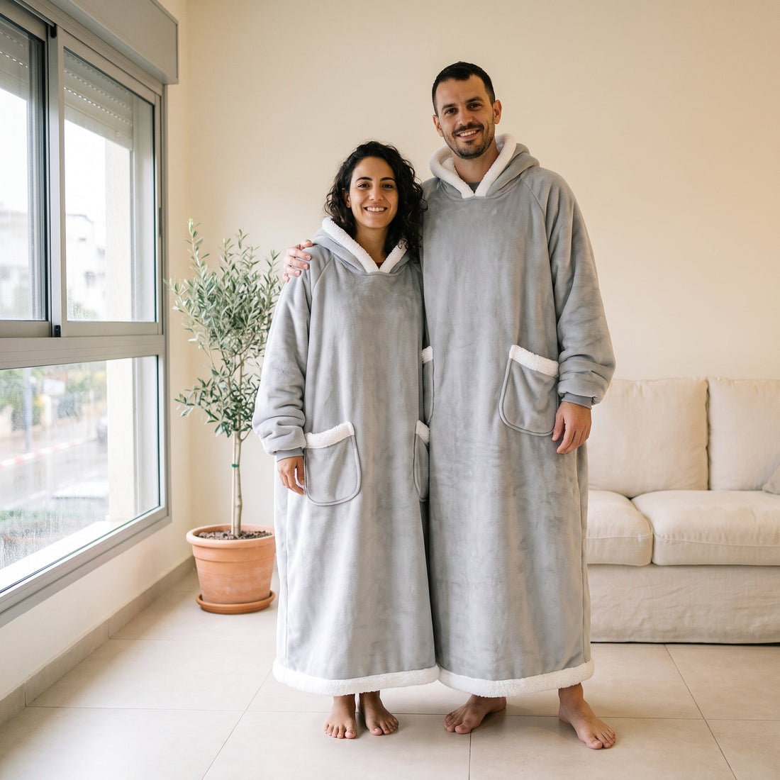 גבר ואישה עומדים בסלון מואר, שניהם בקפוצ'ון שמיכה אפור באורך מלא עם שני כיסים קדמיים